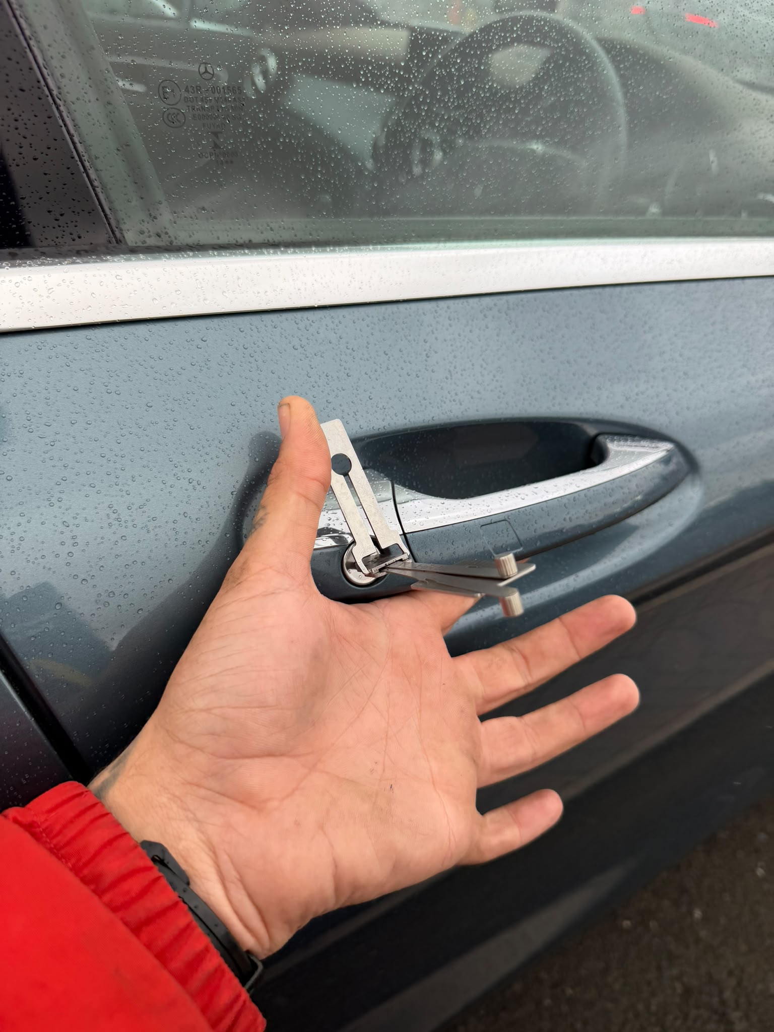Blue car door lock being picked open showing hand turning silver lock pick in car door barrel 