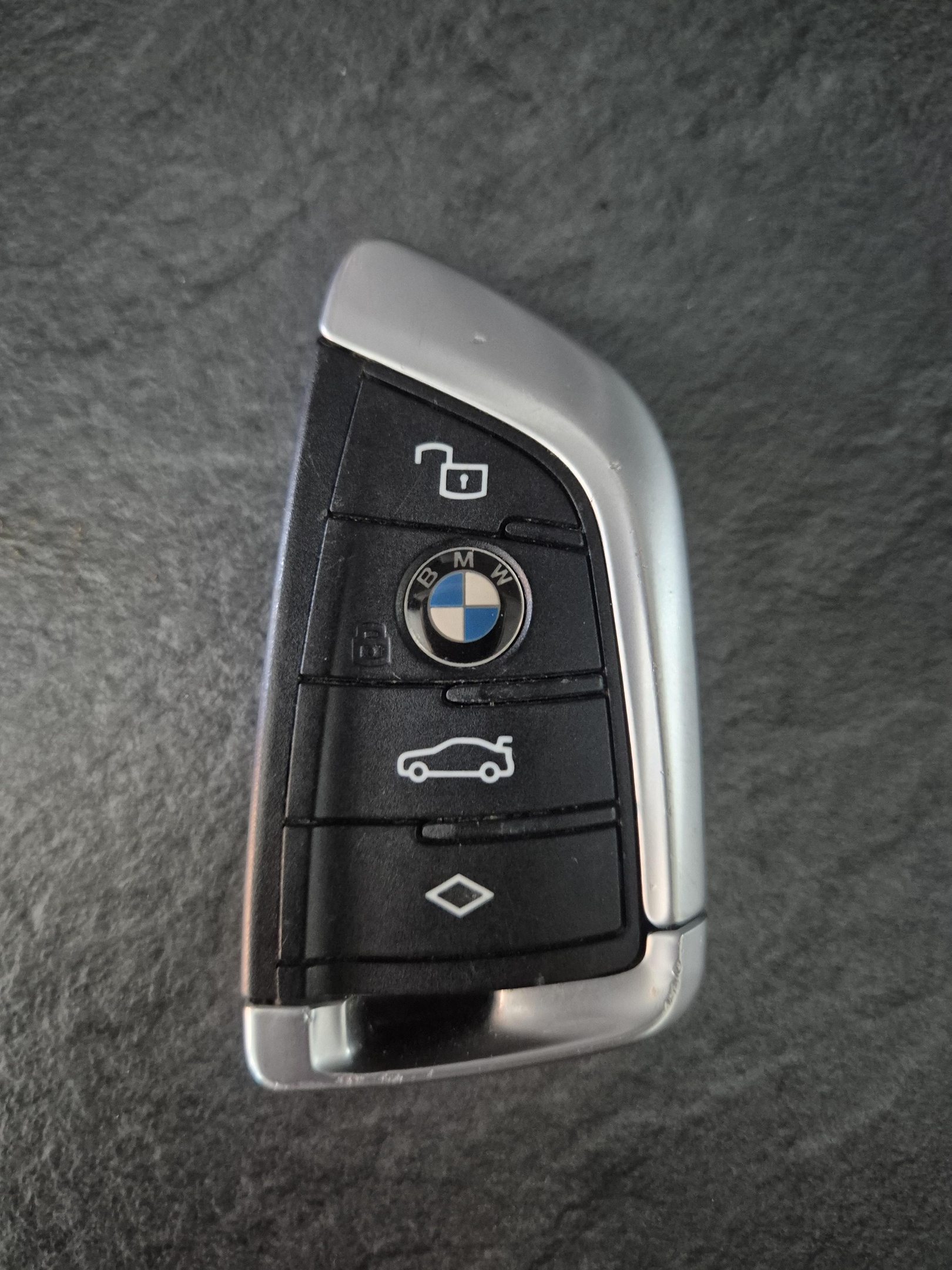 Transponder key fob programmed for 3 series BMW. showing black and silver key on dark green surface.