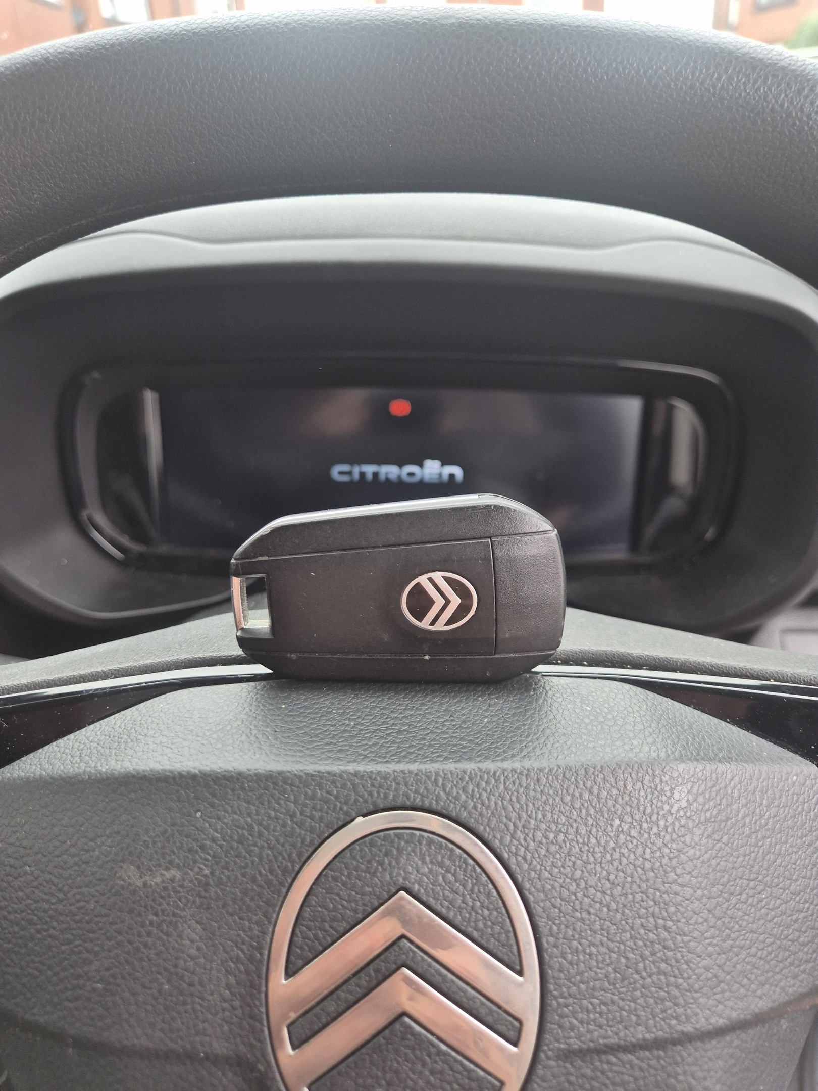 Black Citroen key cut and coded at Whitley Bay seafront. Car key laid on top of black steering wheel with instrument cluster in background 
