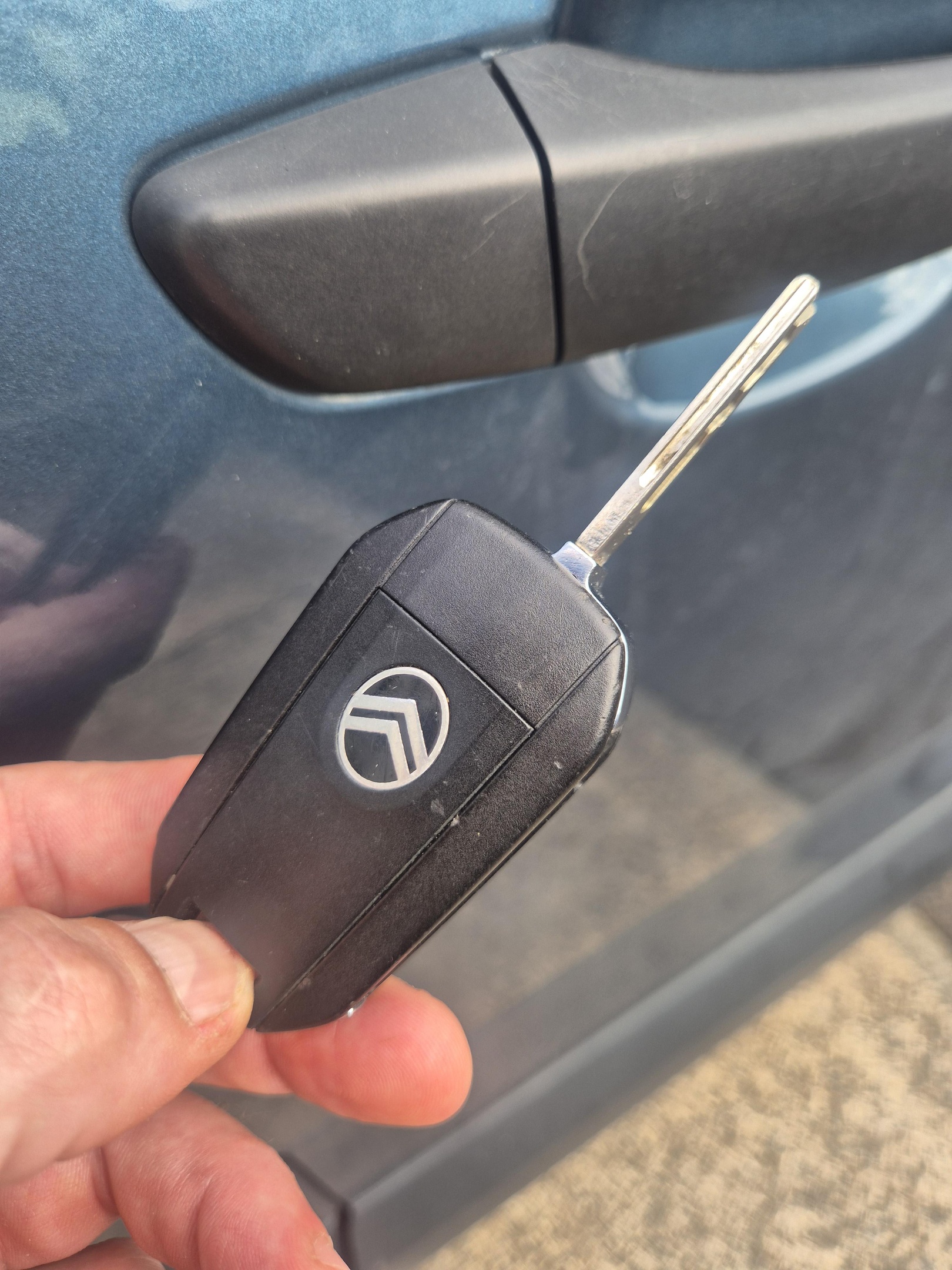 New Citroen Berlingo transponder key fob being held next to green van showing black fob with Citroen logo