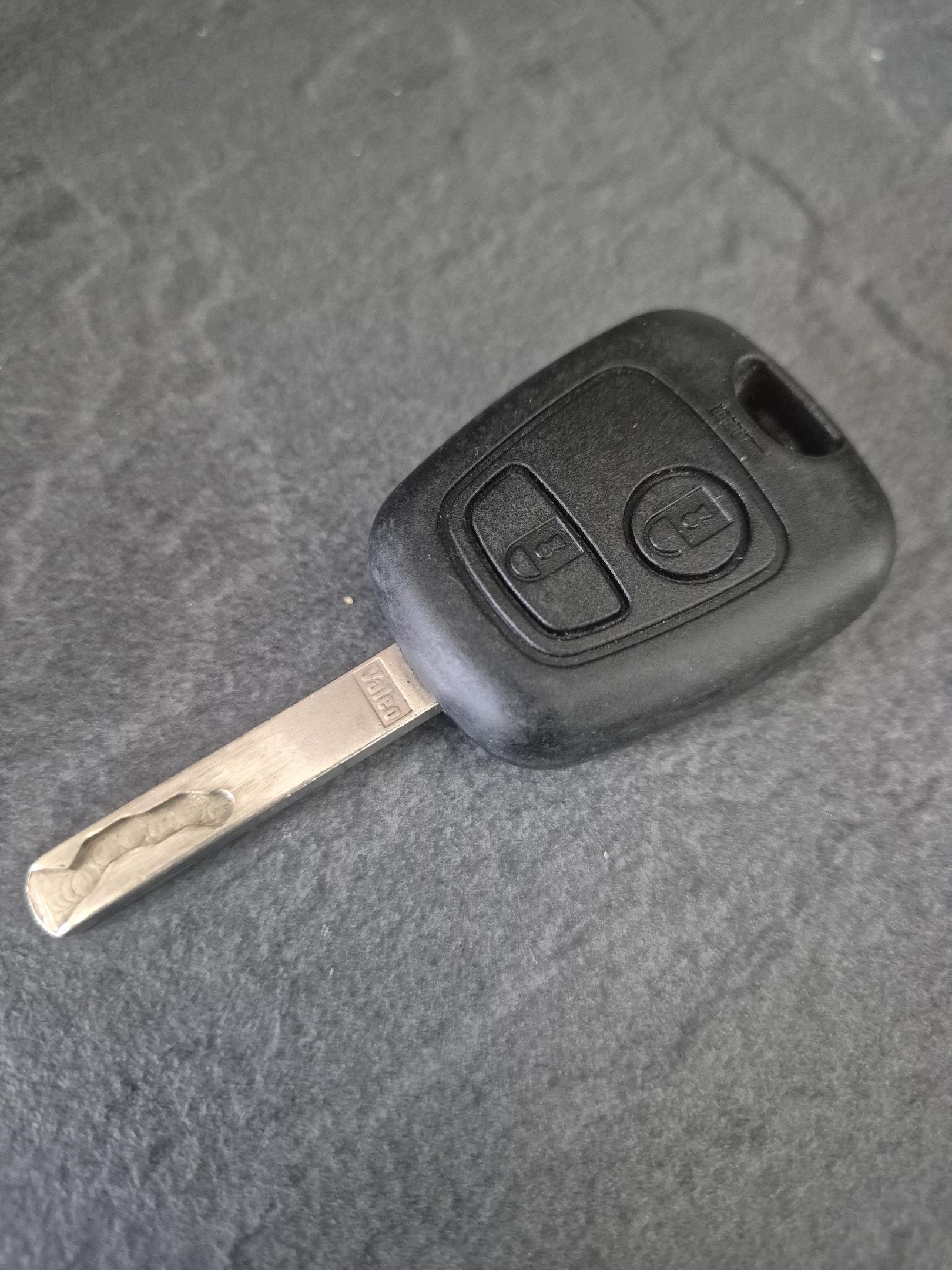Laser cut new car key blade laid on speckled grey surface